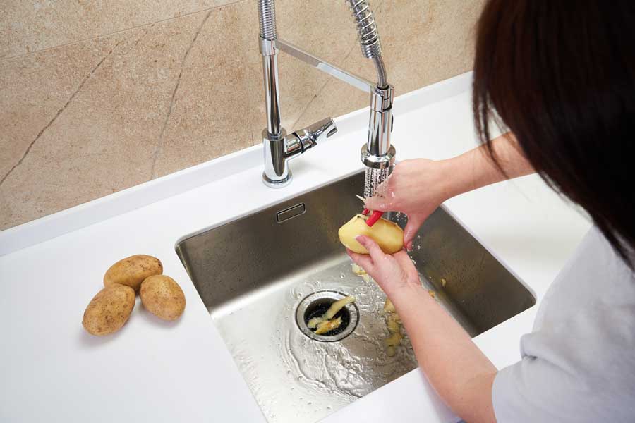 A woman peeling a potato in a sink